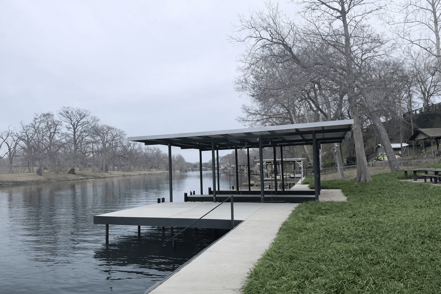 Completed waterfront on the south side of Lake McQueeney &mdash; black steel double boathouse with metal roof, attached concrete swim platform with water entry stairs, and 5-foot concrete sidewalk bulkhead cap